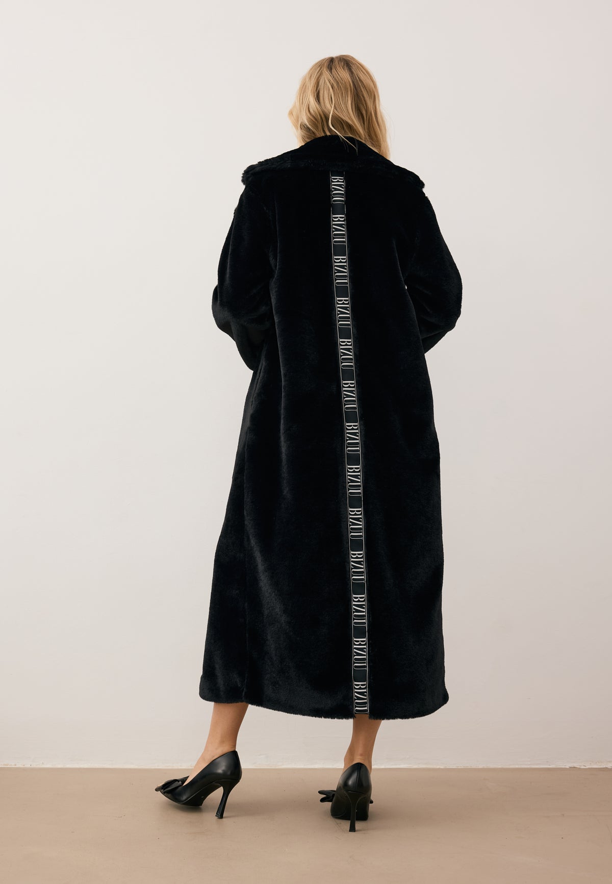 Model standing with her back turned in a long LIVORNO fur coat with a stripe on the back.