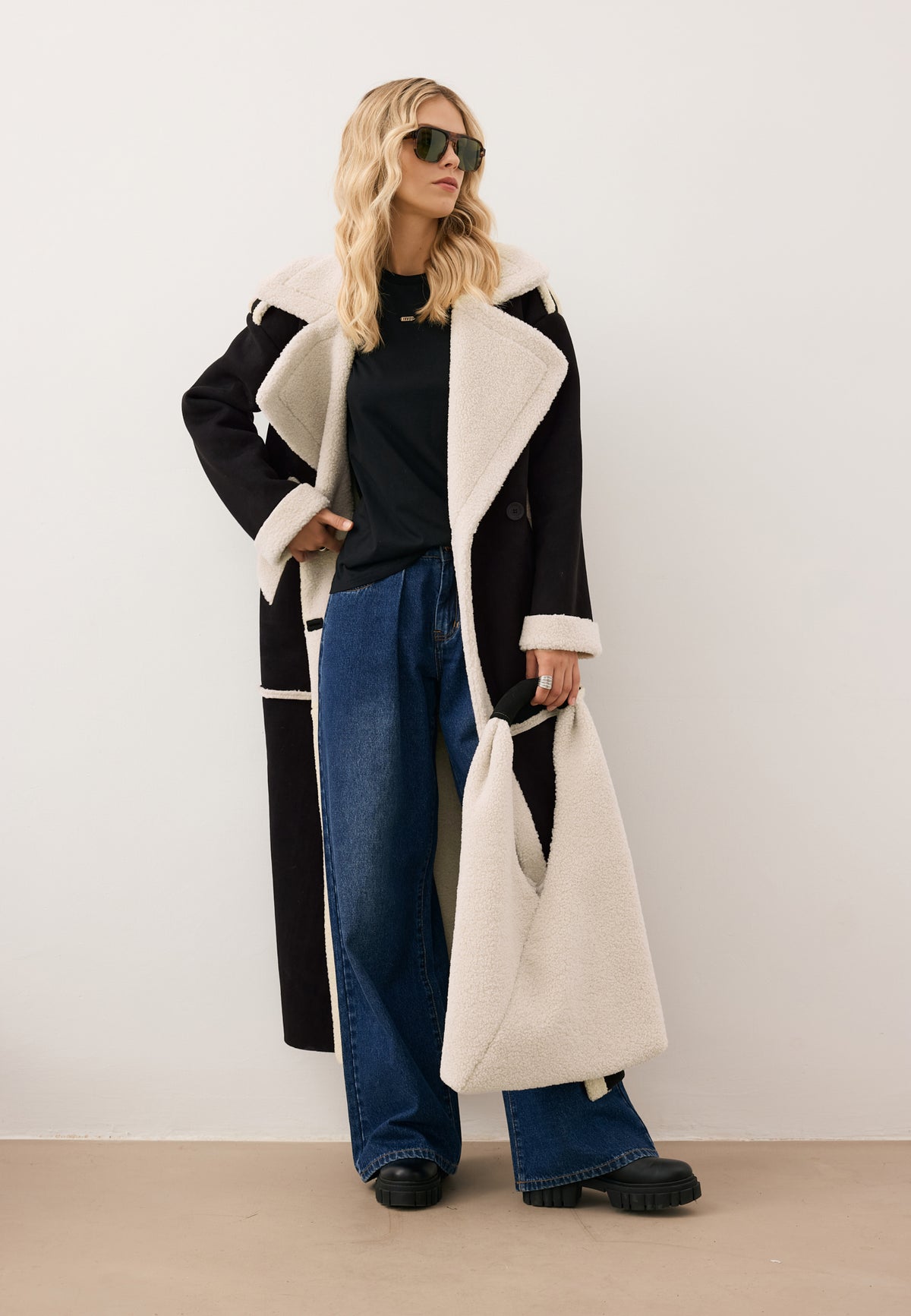 Model looking to the side with one hand on her hip, dressed in the black MAFARA shearling coat, LAYLA jeans, and MISTRETTA sunglasses.