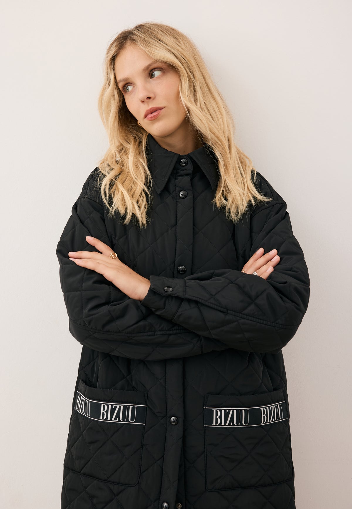 Close-up of the model with folded arms, wearing the black MAREVIA quilted coat with logo detail on the pocket.