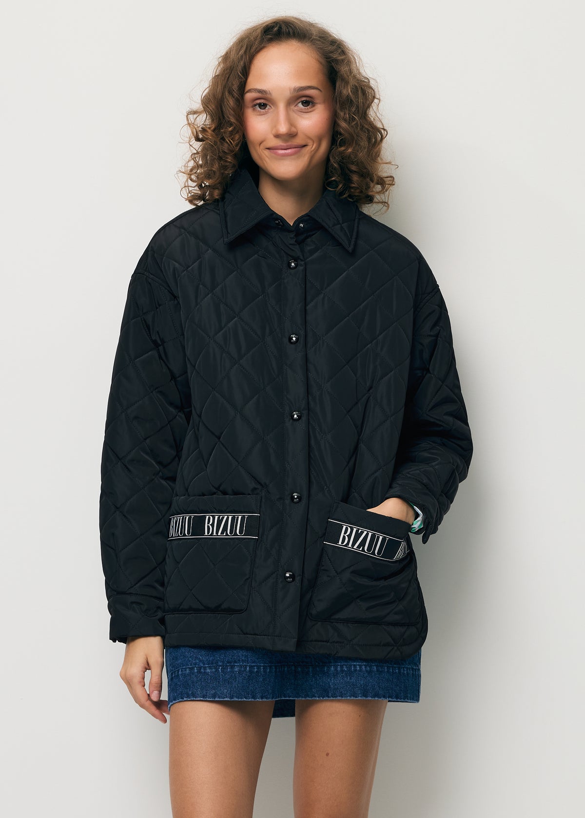 A smiling model with her hand in the pocket of the black quilted MARIN jacket with logo tape on the pocket.