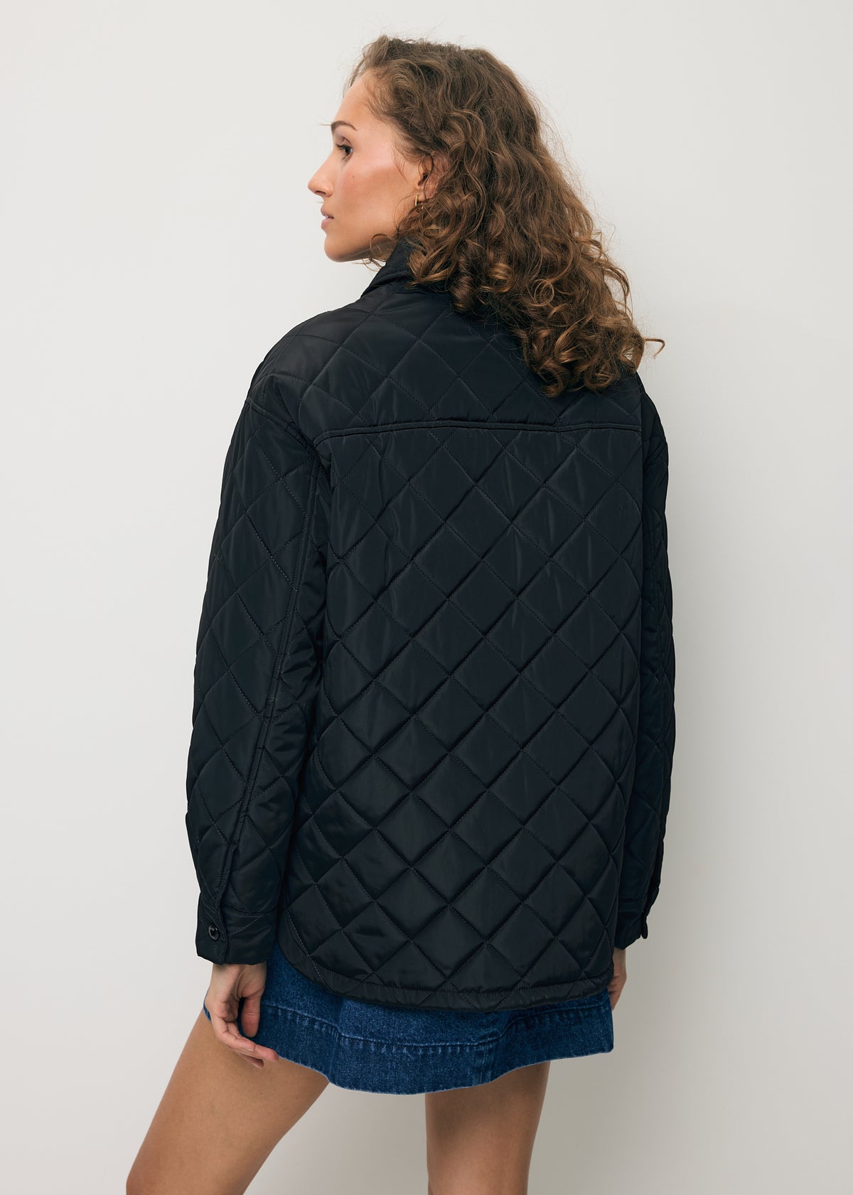 A model standing with her back to the camera, wearing the black MARIN quilted jacket.
