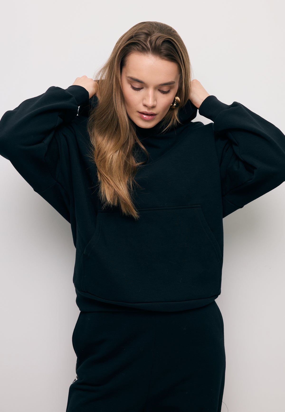 Close-up of the model adjusting the hood, wearing a black MAYRA hoodie with a side stripe on the sleeve.