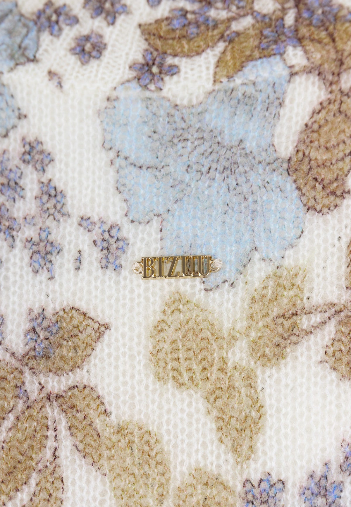 Close-up of the floral pattern and gold logo on the MENTON sweater.
