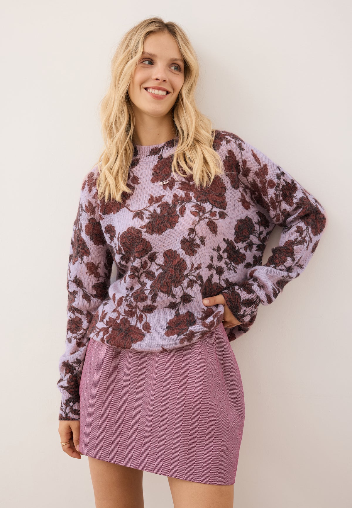 Model with one hand bent at the hip, wearing the pink floral MENTON sweater paired with the burgundy BREDA skirt.