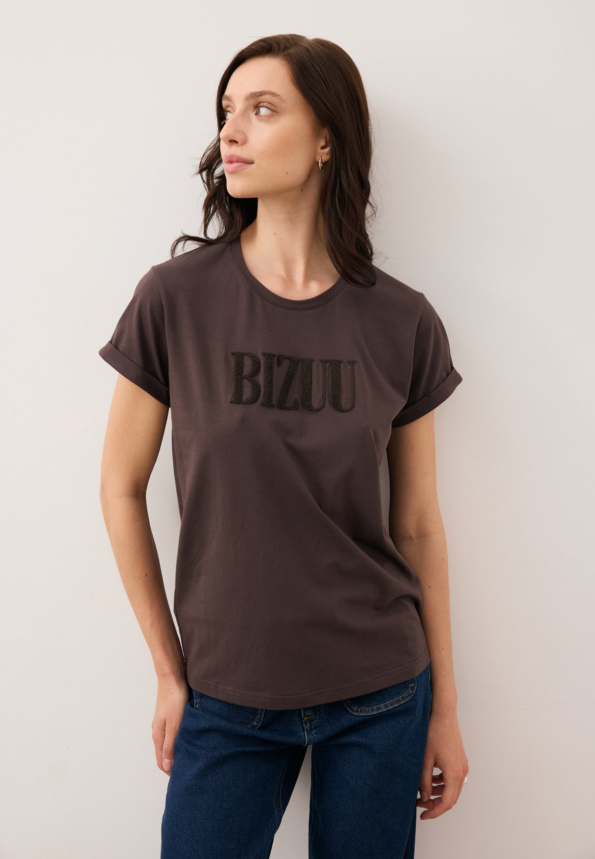 Model looking to the side in the NIKKO T-shirt with front logo in chocolate color.