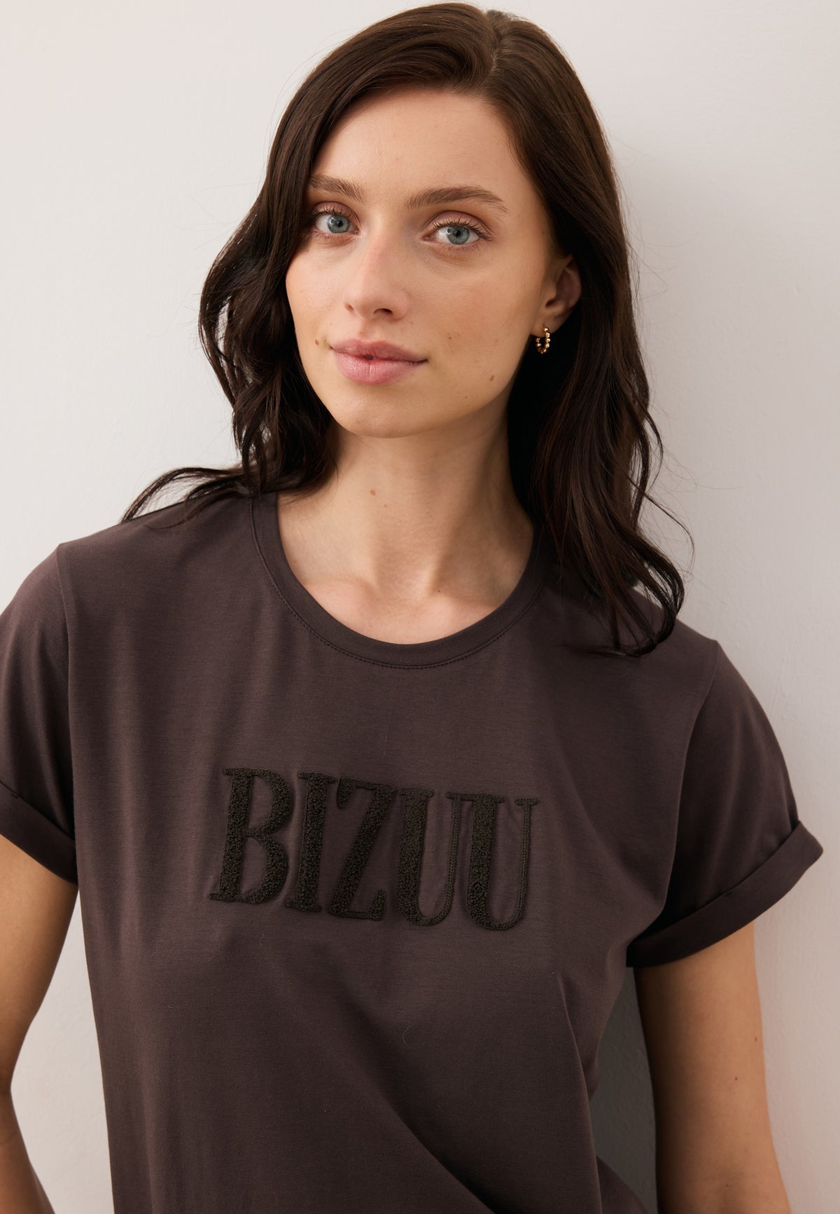 Close-up of the model wearing the chocolate NIKKO T-shirt with brown front logo.