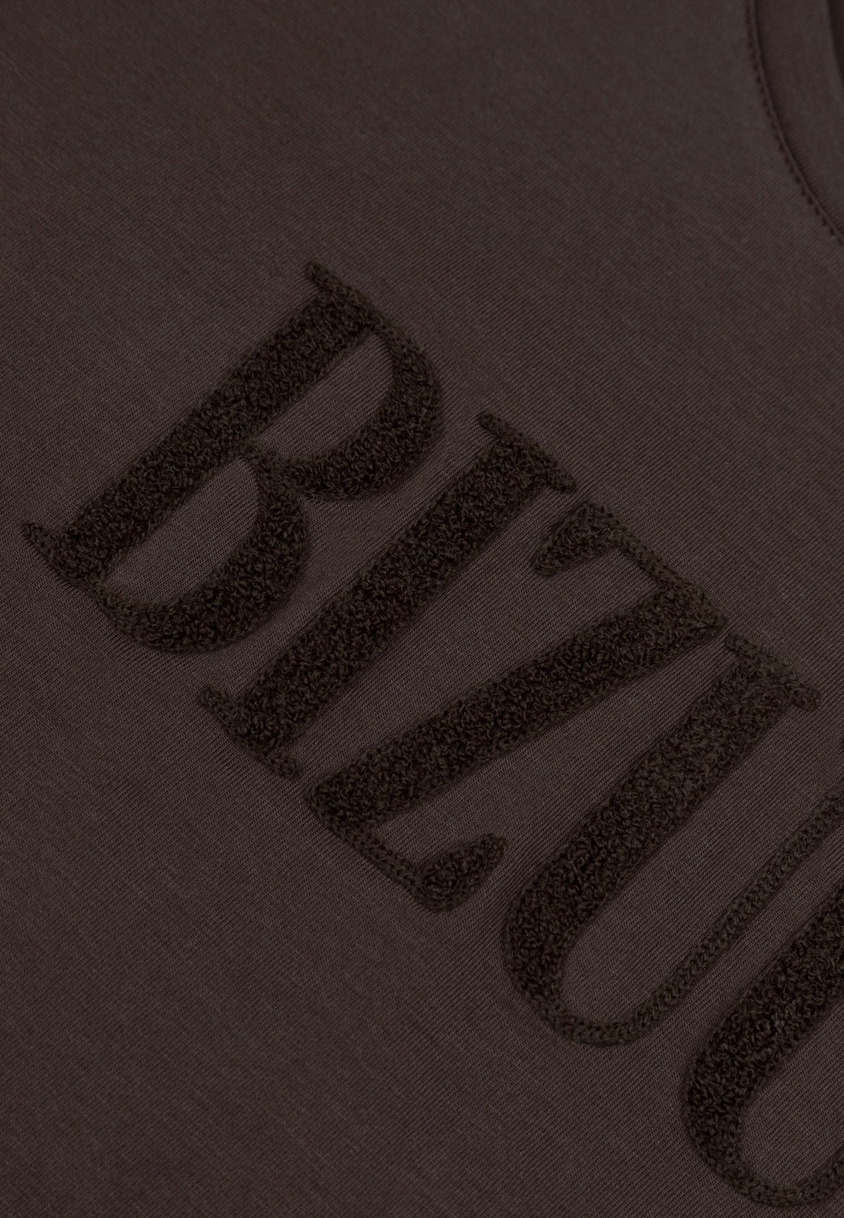 Close-up of the raised logo on the brown NIKKO T-shirt.