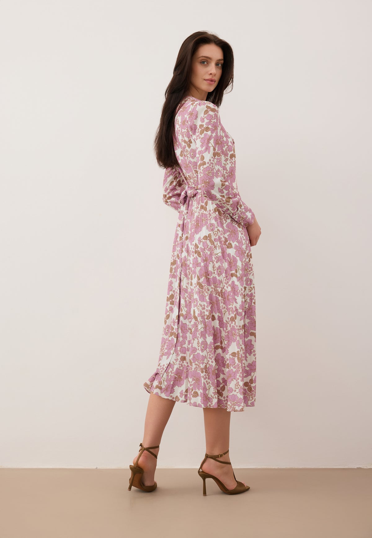 A model standing sideways wearing a NYLA dress with a pink print.