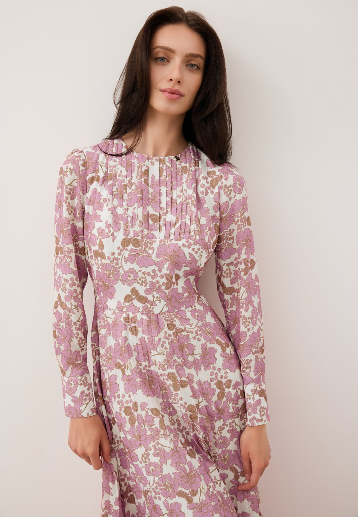 Close-up of a model leaning against a wall, wearing a NYLA dress with a pink floral print.
