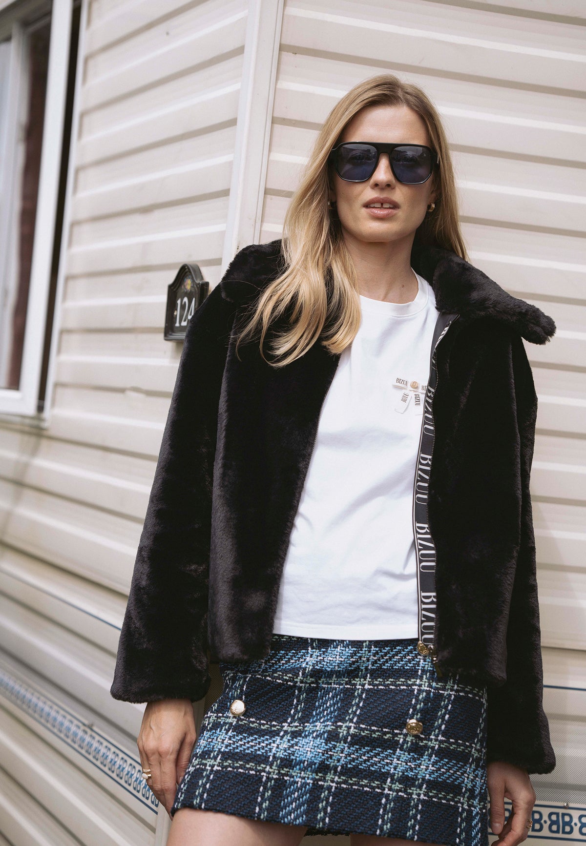 Model leaning against a wall, wearing the PIACENZA short faux fur jacket unzipped, with branded tape along the zipper.