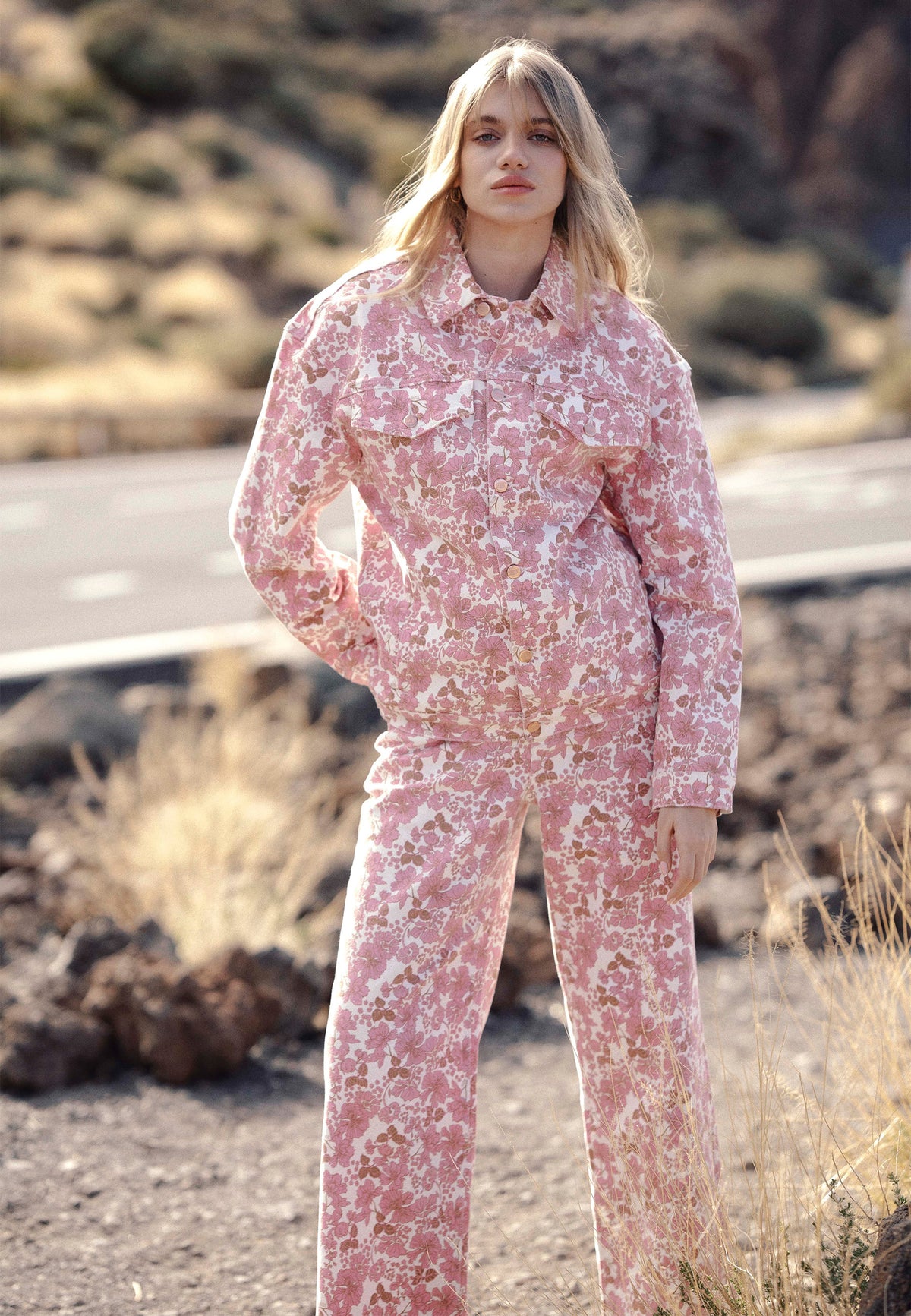 A model leaning against a wall, wearing a denim set in a floral print: the PRINSA jacket and DONY trousers.