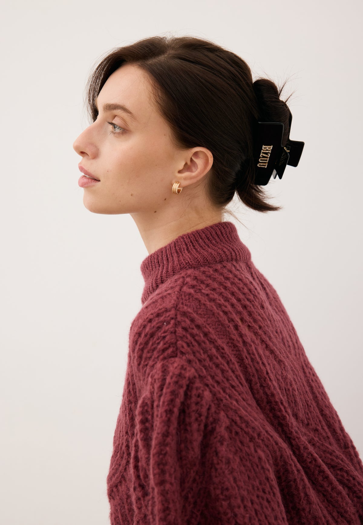 Model standing in profile with her hair pinned up using the black rectangular RHODI hair clip featuring a rhinestone logo.