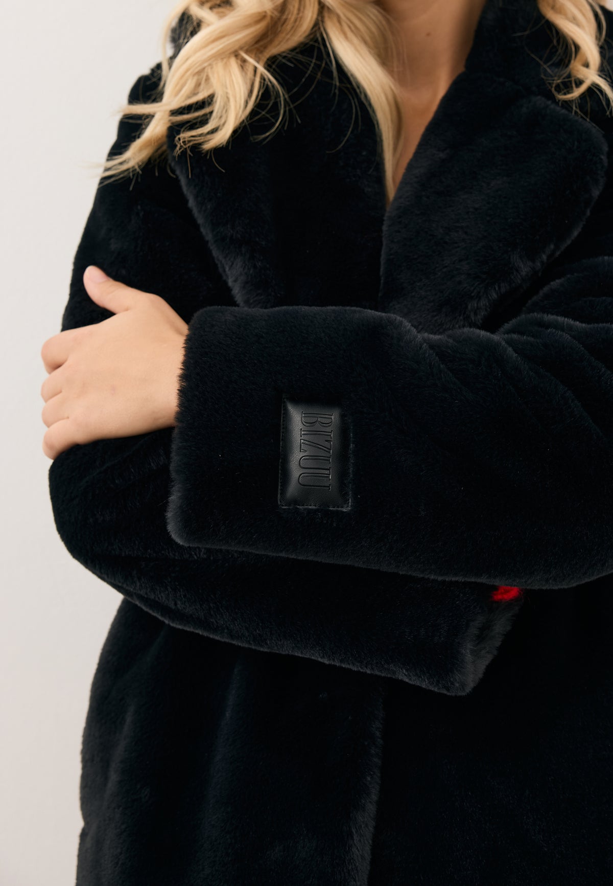 Close-up of the model’s crossed arms, showcasing the black ROMA coat with embossed sleeve logo.