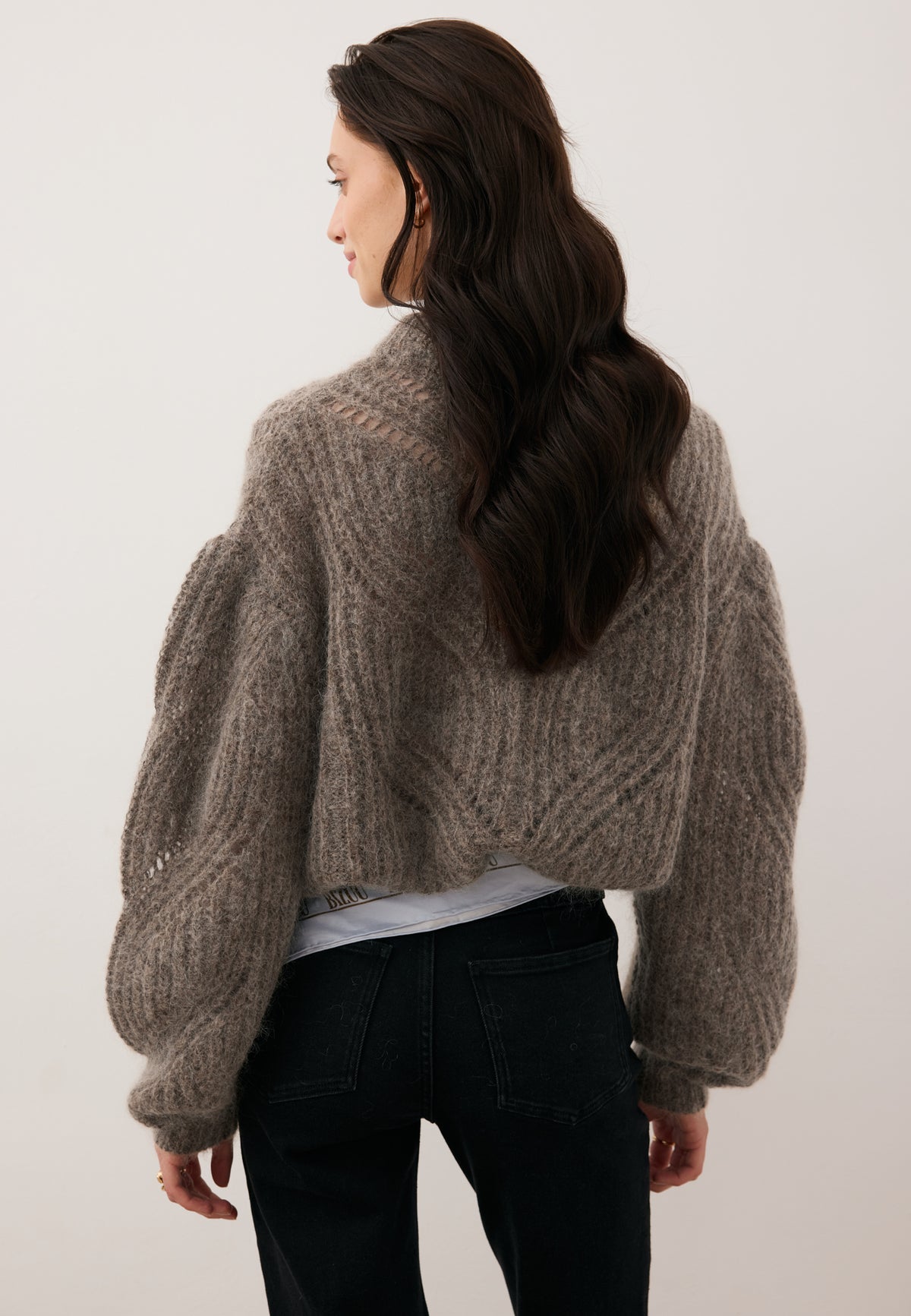 Model standing with her back to the camera in the beige ROSSO openwork sweater.