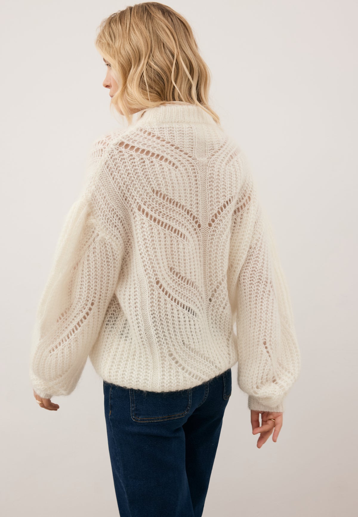 Model standing sideways, showcasing the openwork knit on the back of the cream ROSSO sweater and its puffy sleeves.