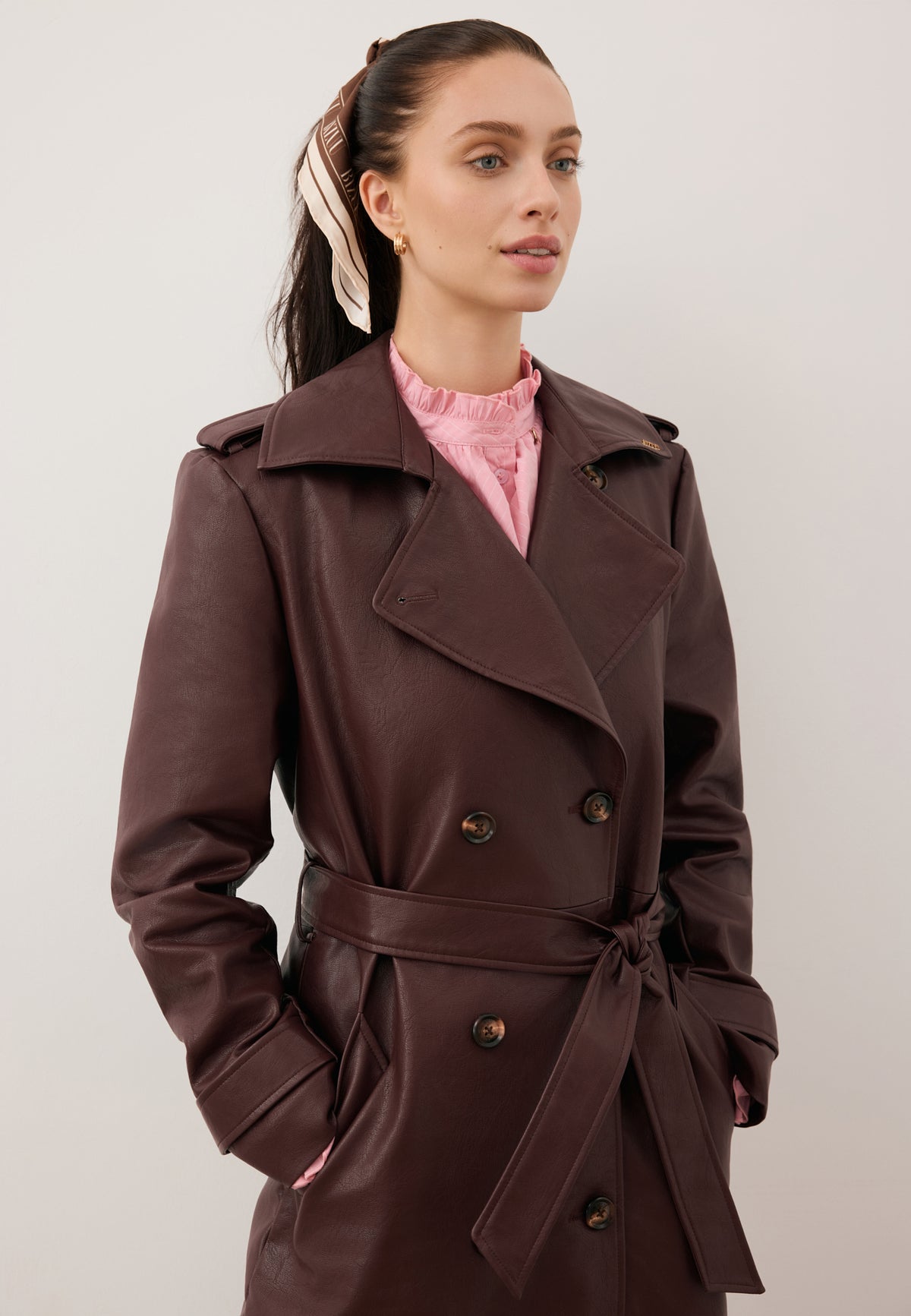 Close-up of a model wearing a brown VENEKIA eco-leather coat and a pink SANNI shirt.