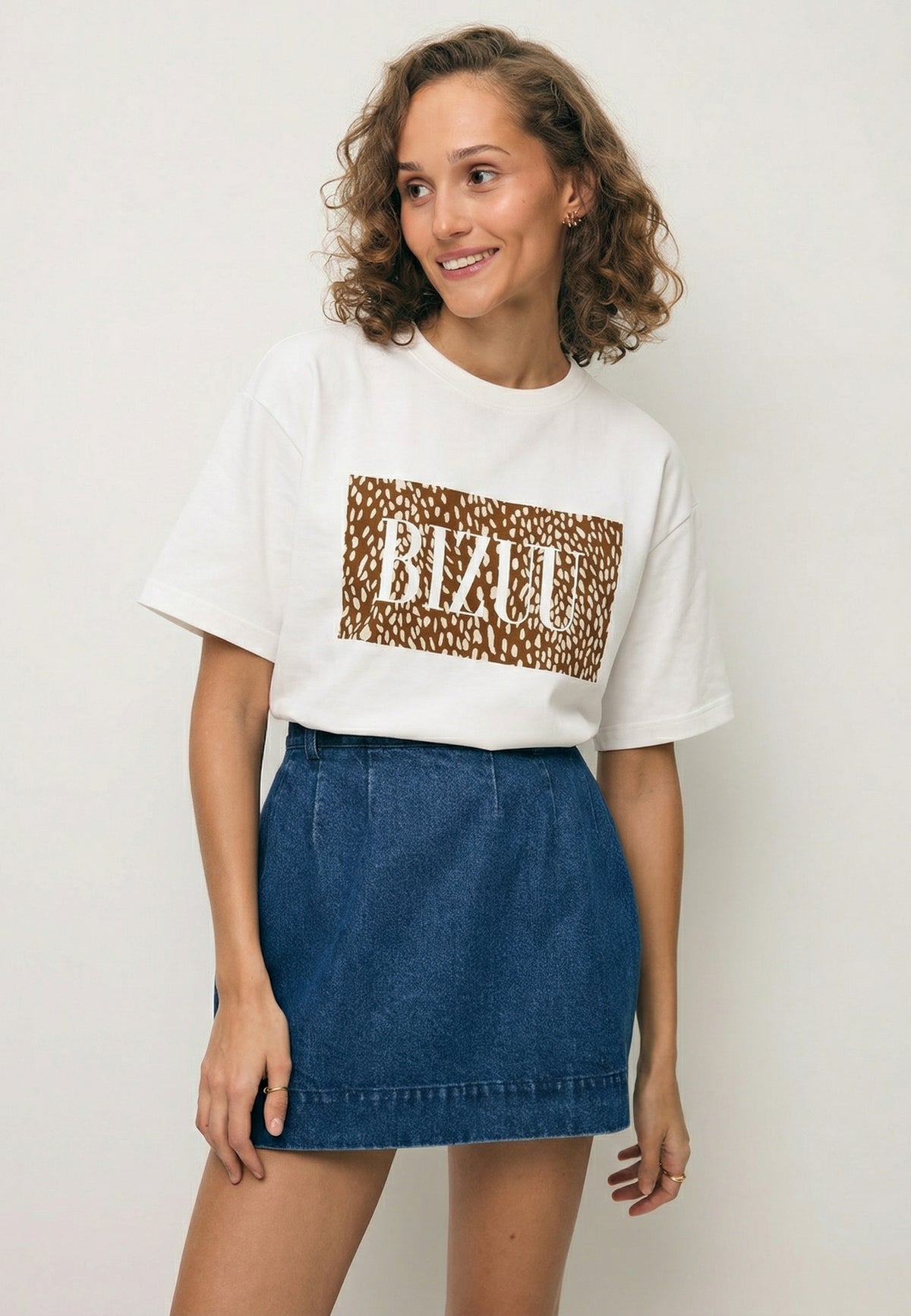A model wearing the SIME cream T-shirt with an animal motif and the BREDA denim skirt.