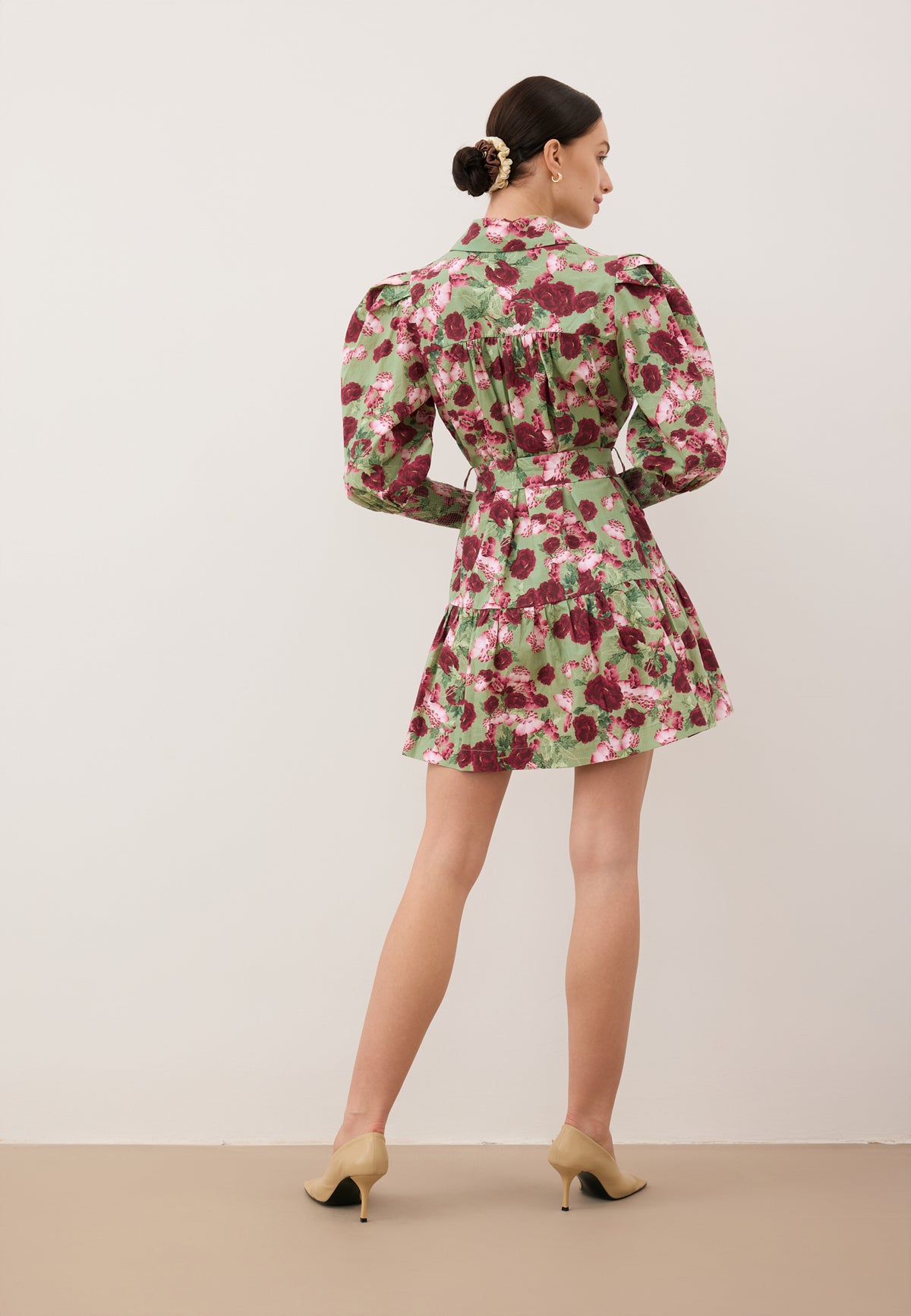 A model standing with her back to the camera against a white wall, wearing a green mini dress by SOREZIA.