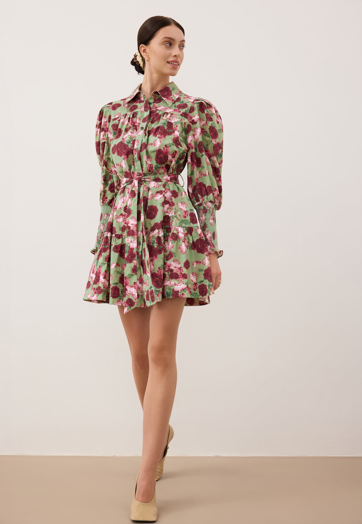 A model against a white wall wearing a green SOREZIA mini dress with a floral print.