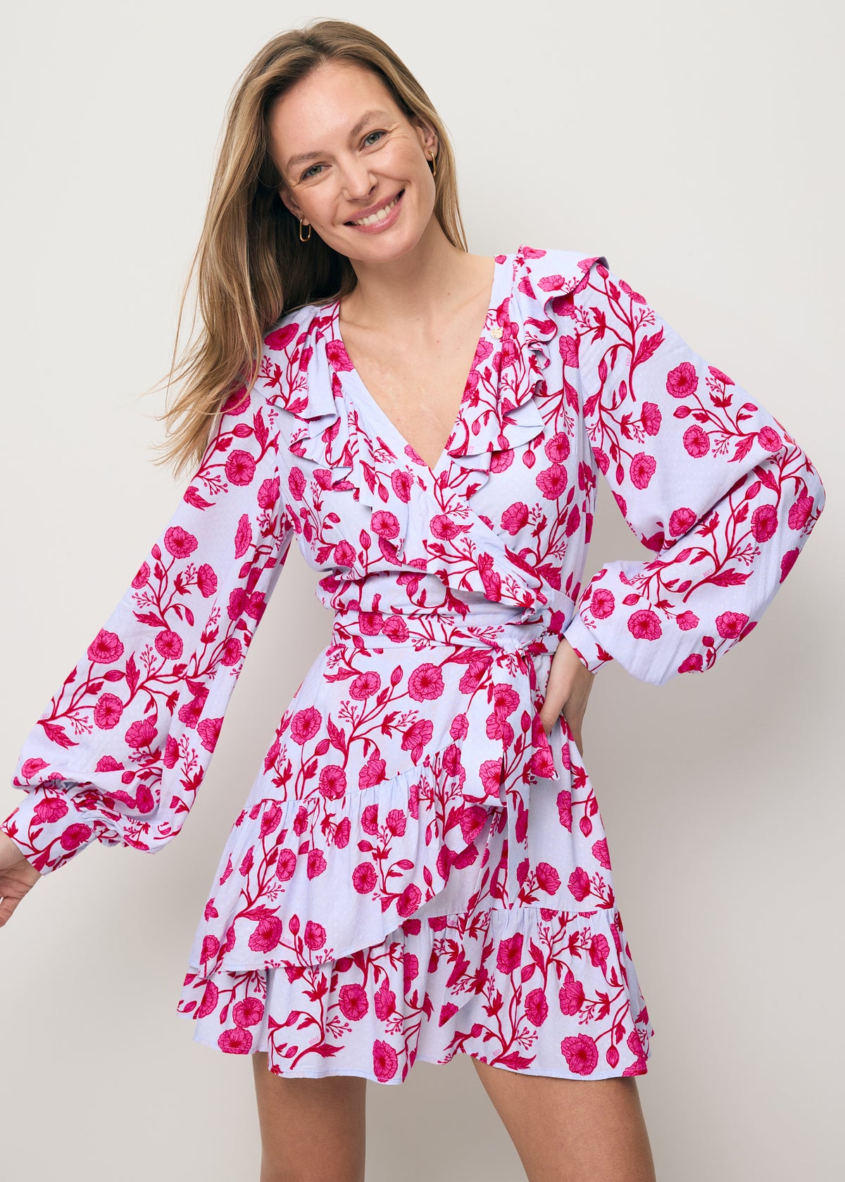 Close-up of a smiling model wearing the SYMA mini dress with decorative ruffles.