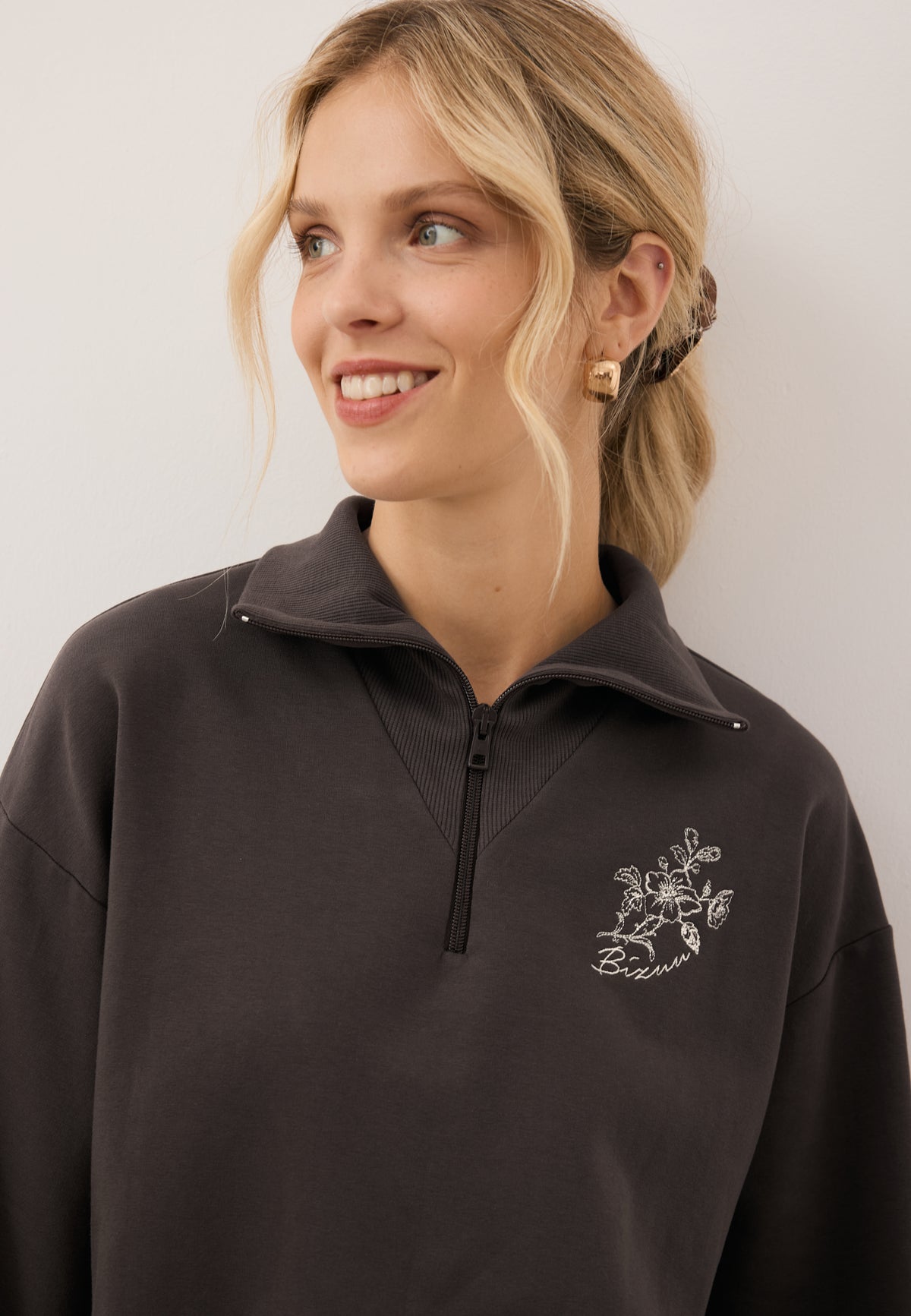 Close-up of the front logo appliqué on the chocolate-colored TANSY sweatshirt.