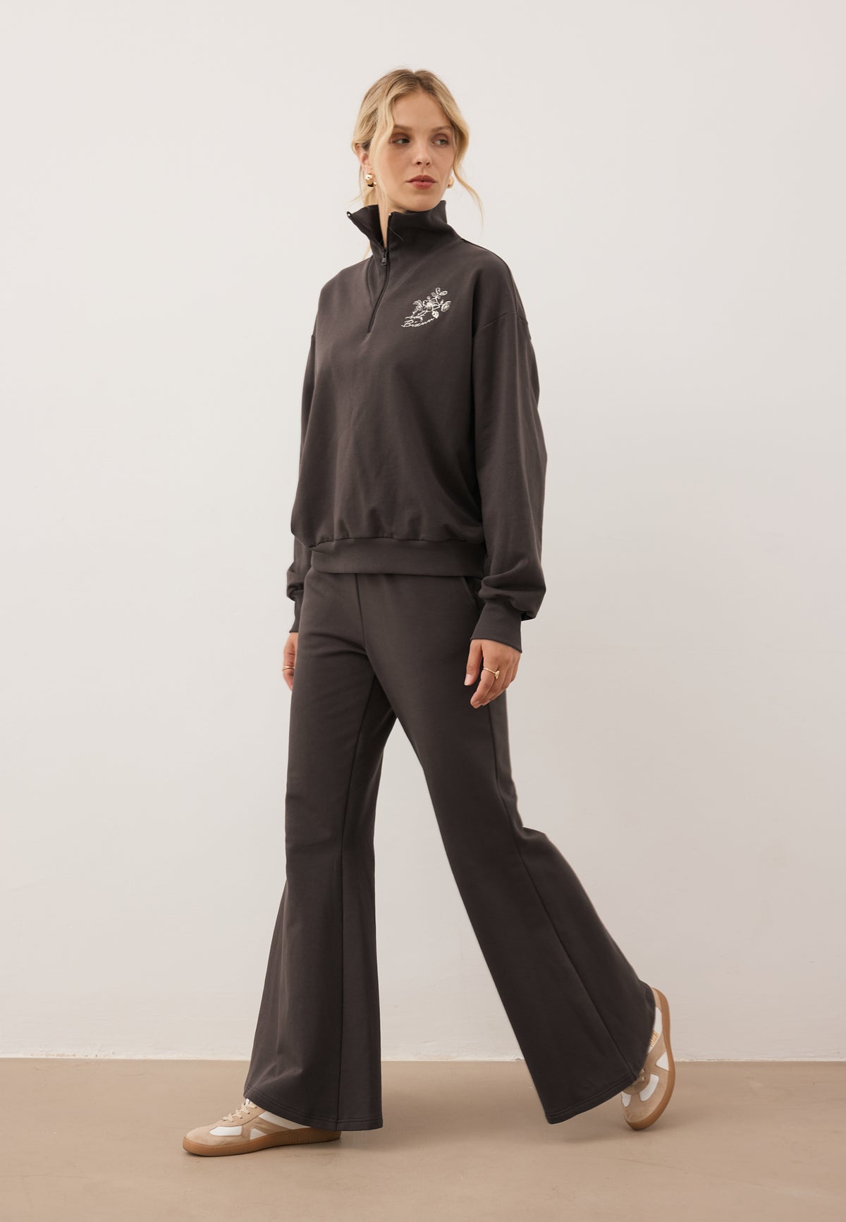 Model stepping forward and looking to the side, dressed in the dark brown tracksuit set – TANSY sweatshirt and ZEIA trousers.