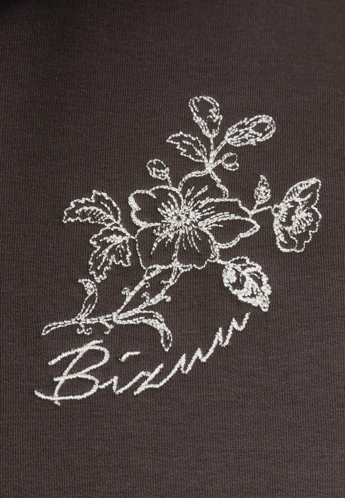 Close-up of the embroidered logo on the front of the TANSY sweatshirt.