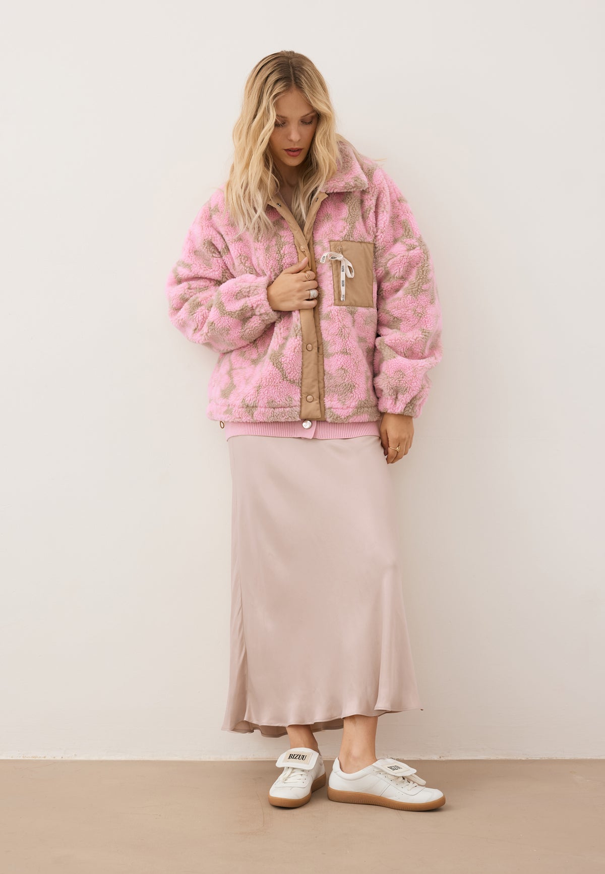 Model looking down, wearing the TEDDY floral fleece jacket, the beige BREE skirt, and MOBBY sneakers.