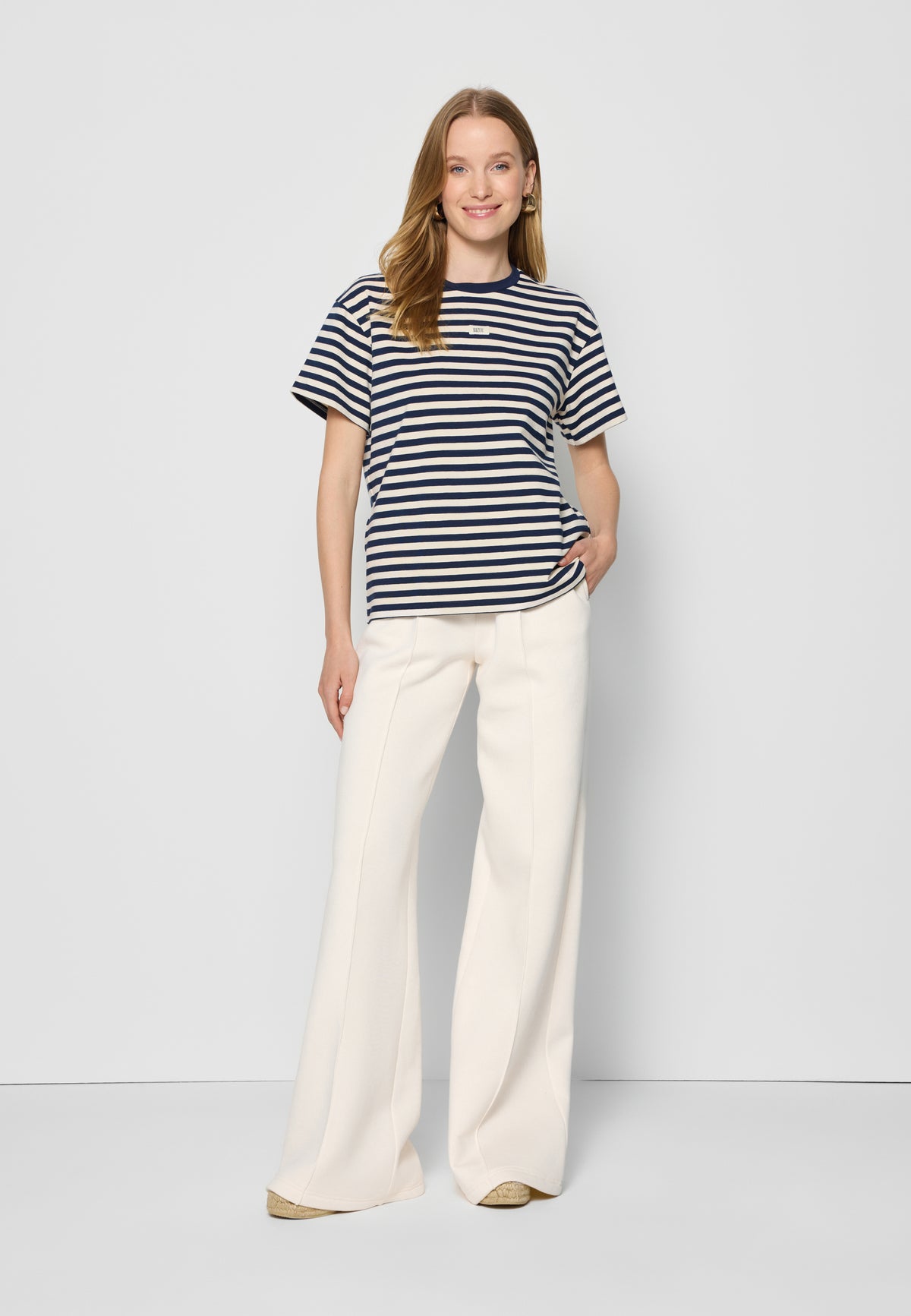 A smiling model on a white background wearing a TISHALLY navy and cream striped T-shirt and PETRA cream sweatpants.