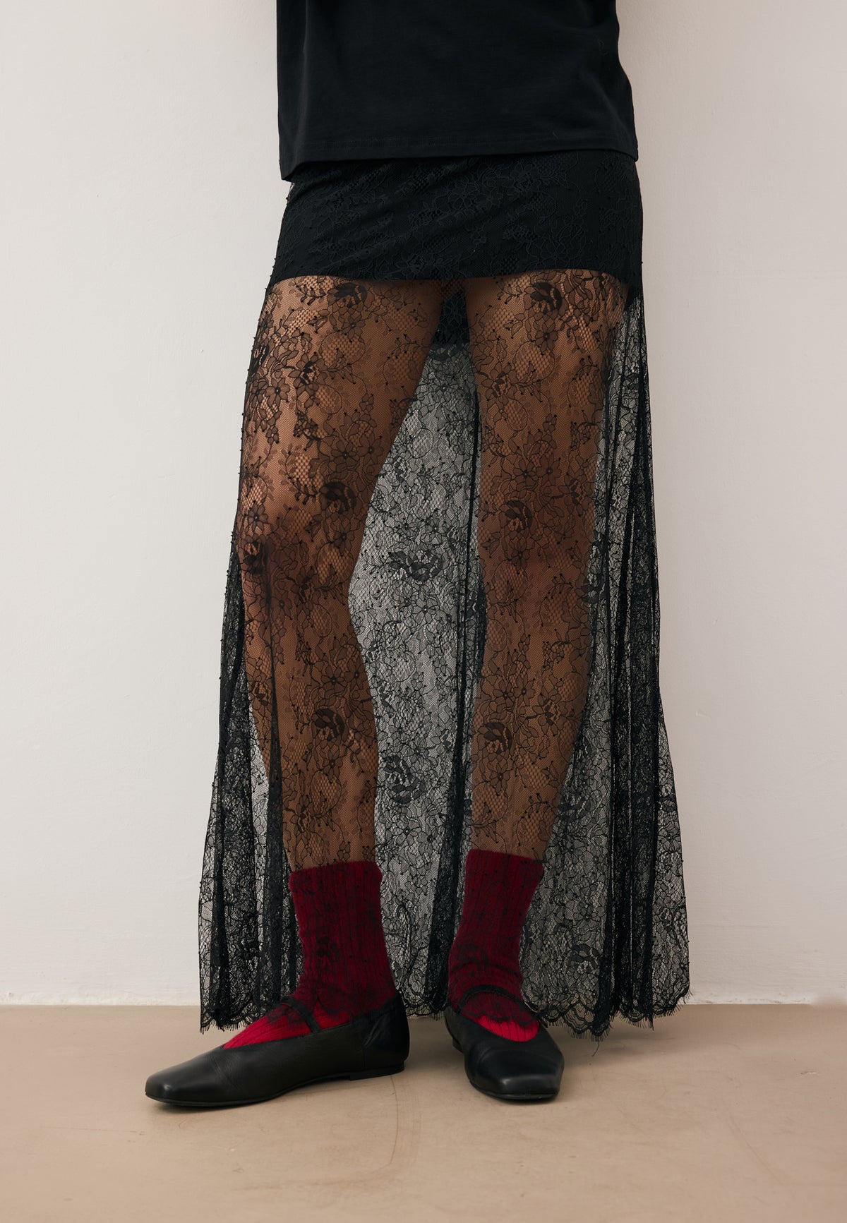 Model with one hand on her hip, wearing the black lace FLACE maxi skirt, black cotton TISHAL T-shirt, and sunglasses.