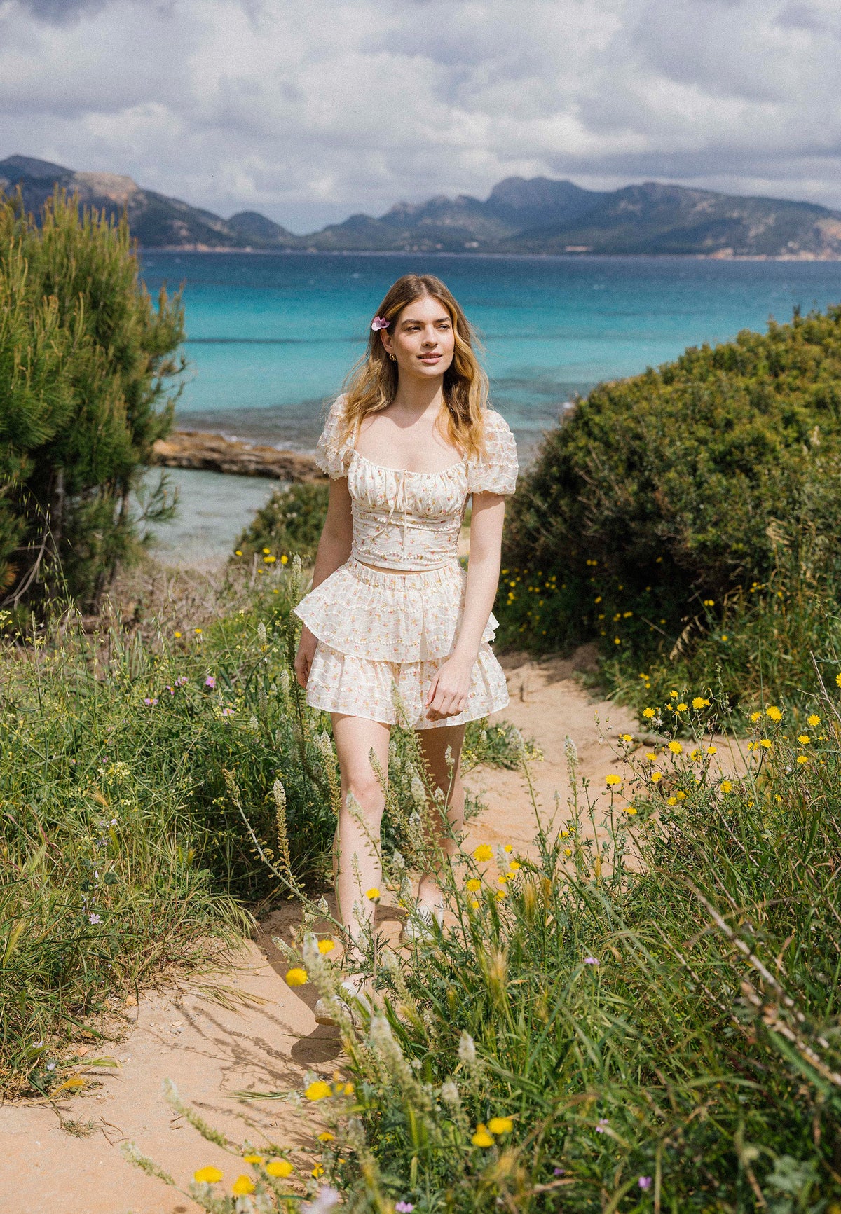 A model in a two-piece set with a delicate floral pattern VANNES and COKO walks barefoot among wild flowers and grasses.