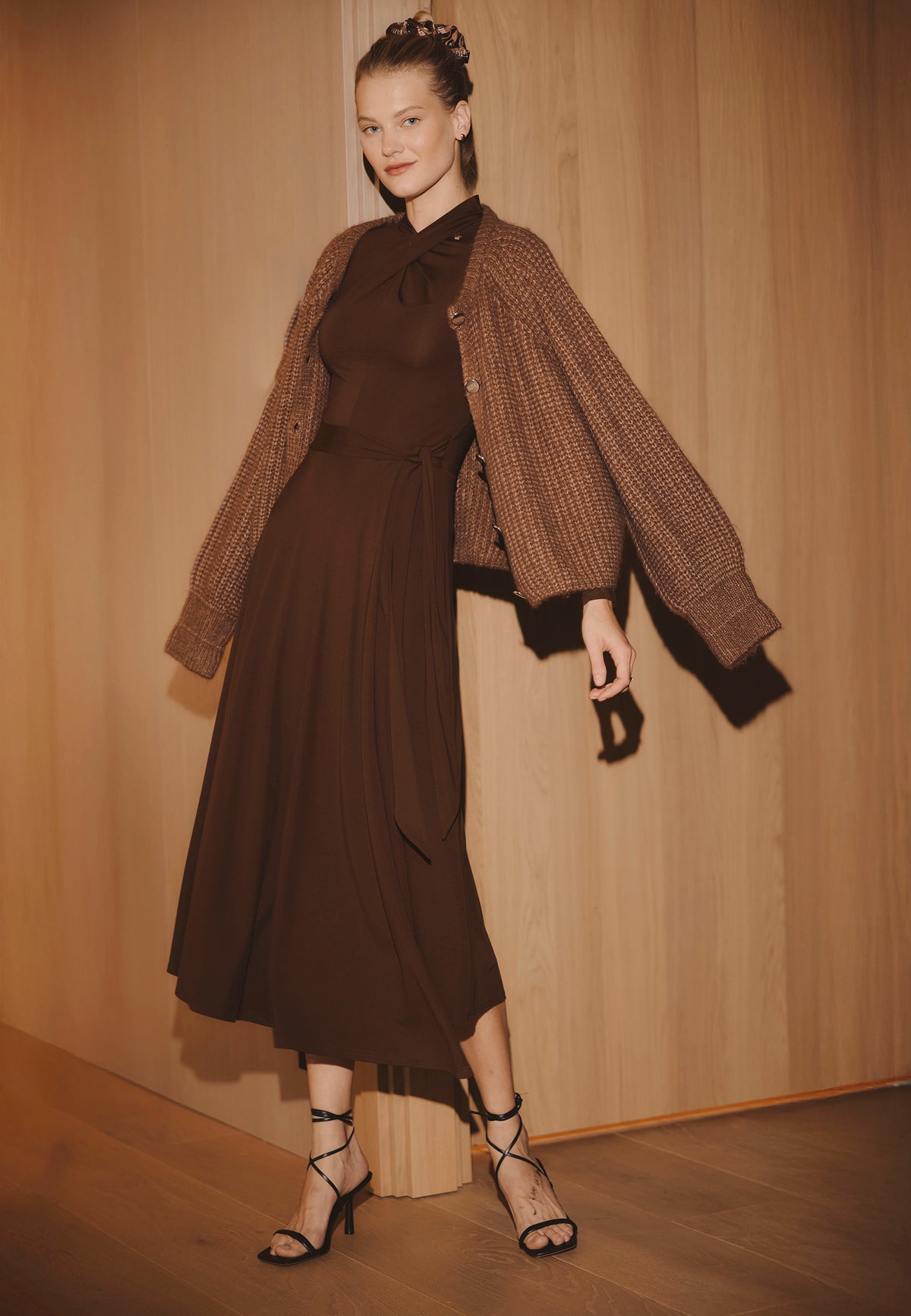 Model standing against a wooden wall wearing the brown knit ROTTA dress paired with the ORNAMY cardigan.