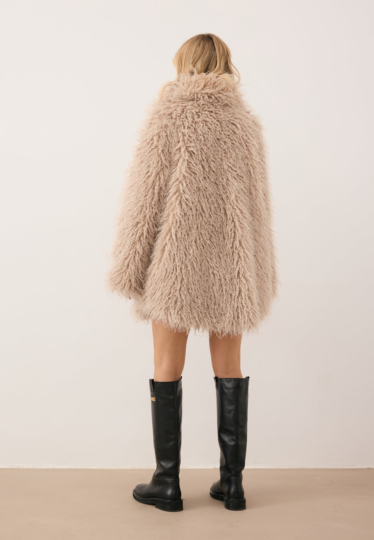 Model standing with her back to the camera, wearing the beige long-hair VICENZA coat.