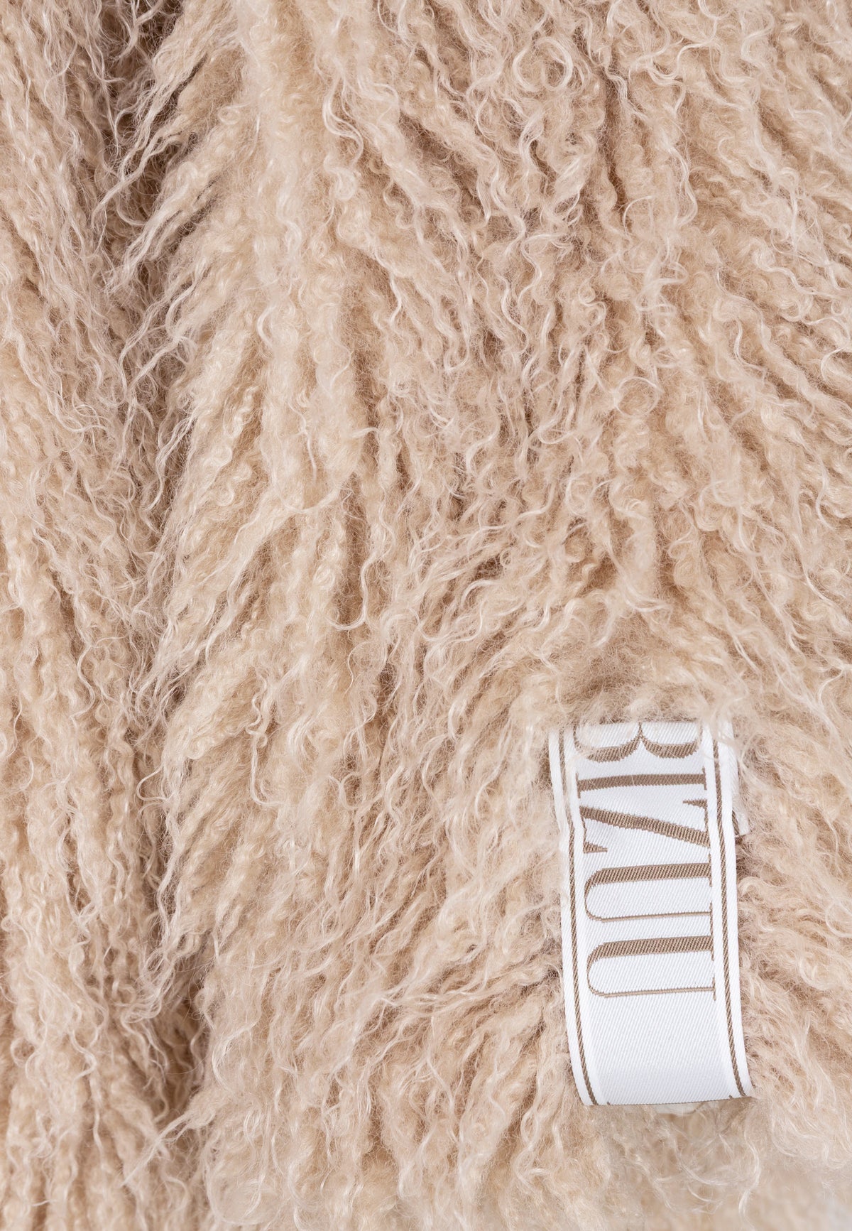 Close-up of the logo label on the sleeve of the beige crimped VICENZA faux fur coat.