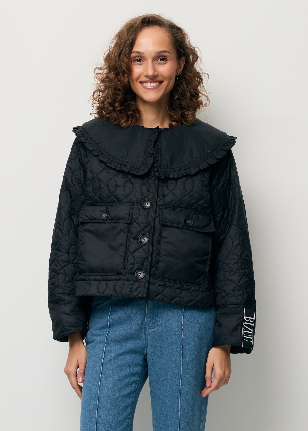 A smiling model wearing a black ZANNI jacket with a detachable collar.