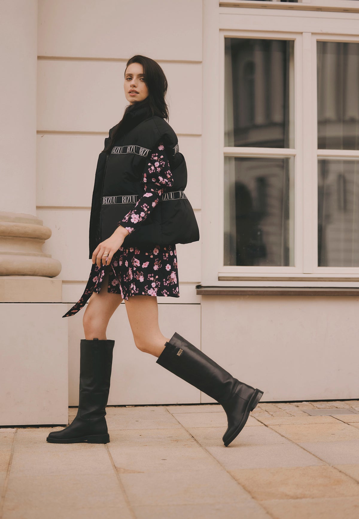 Model walking down the street wearing the AYASE down vest, GEORGINA dress, and CALYX leather boots.