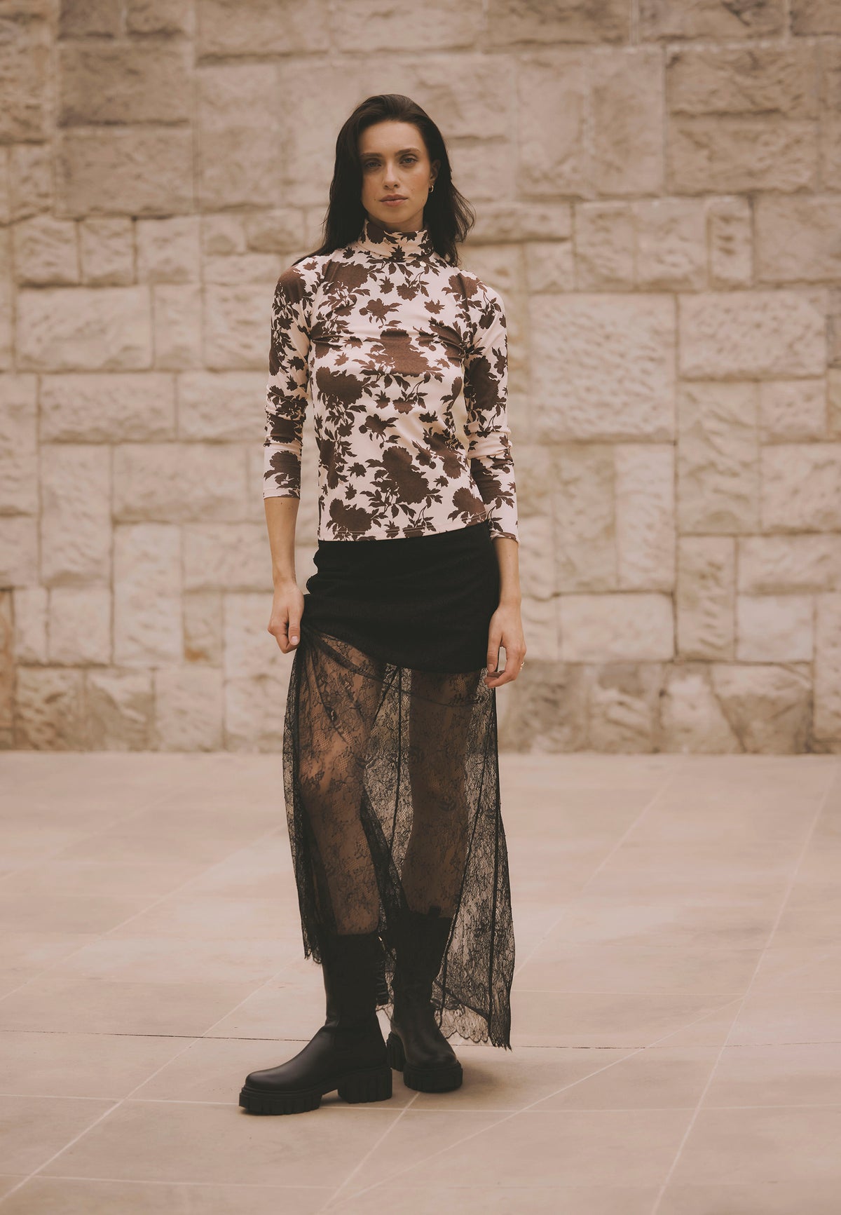 Model standing on the street wearing the beige OWAKA turtleneck and the black lace FLACE maxi skirt.